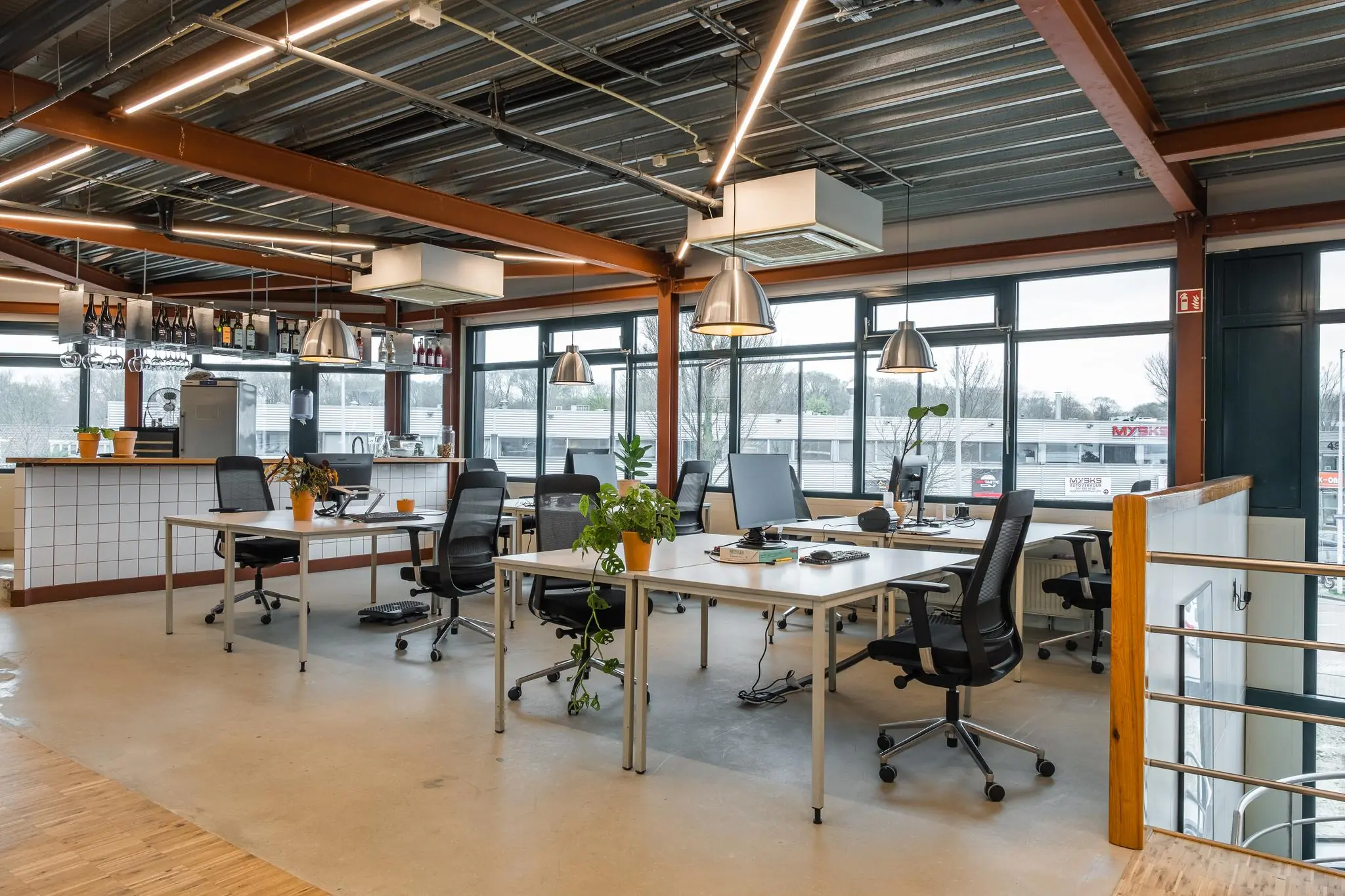 Modern kantoorinterieur aan de Johan van Hasseltweg met open werkplekken, veel daglicht en een bar met flessenrek.